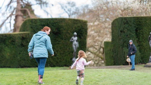A woman and a young girl running through a garden at Chirk Castle, participating in an Easter trail.